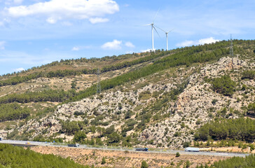 Fototapeta na wymiar Mountains landscape. Eolic park windpower. Wind farm, Wind green energy. Wind turbines, Windmill power generation. Freight shipping. Semi truck with Semi-trailer driving on highway in Castellon, Spain