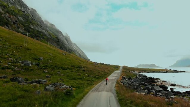 Camera follows cyclist riding bike in incredible epic landscape surrounded by mountains and fjord. Gravel cycling on dirt unpaved road in natural park