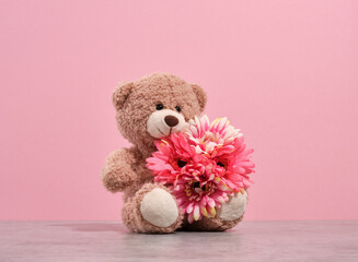 A soft cheerful teddy bear sitting with bright beautiful flowers. Play fun time.