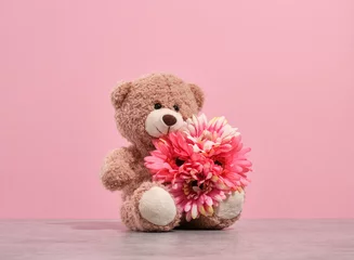Fotobehang A soft cheerful teddy bear sitting with bright beautiful flowers. Play fun time. © Dima