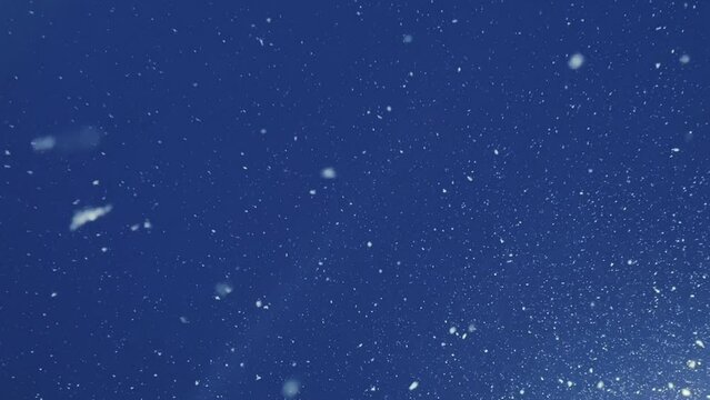 Falling snow in the light. Flying snow on a dark blue background. Snow-covered sky. Snow movement in 4K format. The view of falling snow against the light of a glowing lantern at night.