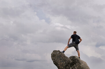 Young man standing on a rock at the top of a mountain peak looking ahead the inmense sky on a...