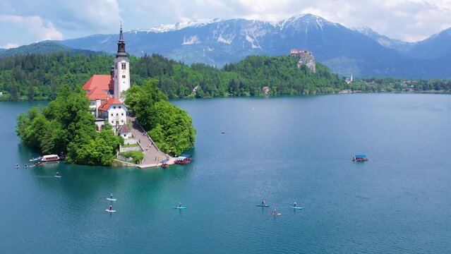 Aerial view of Church of the Assumption of Mary in the center of the lake Bled. Flying around small island on Bled Lake in Slovenia, warm summer day sun