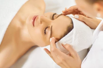 Fototapete Spa Close up happy young woman with soft white towel on head relaxing at luxury spa salon and enjoying facial massage done by professional beautician or cosmetologist. Beauty treatment, skin care concept