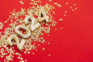 2024 gold colored numbers and glitter confetti on a red background. New Year composition