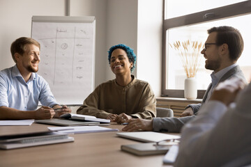 Cheerful diverse business team brainstorming on creative project, discussing ideas, laughing, talking at meeting table in boardroom, having fun, relaxing, enjoying teamwork, success, group creativity