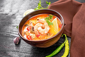 Soup Tom Yum with lemons in bowl on dark wooden board