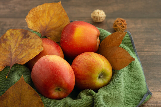 Red apples in autumn foliage. Bright apples on a kitchen towel surrounded by dry autumn leaves. Apples on a wooden background for a decorative picture on the wall.