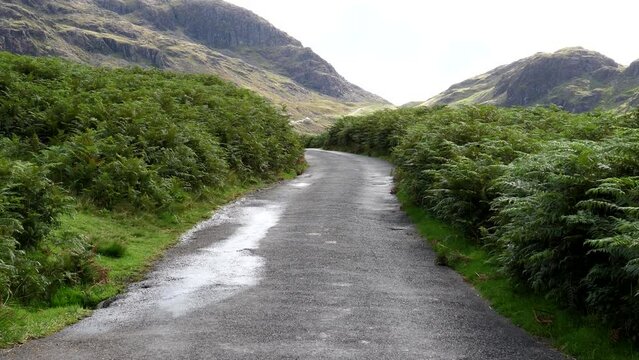 Three cars driving down winding single lane road from 
Hard Knott Hardknott Pass to Eskdale in mountains of Lake District, England, UK.
