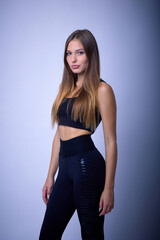 Portrait of a beautiful confident athletic woman with long hair leading a healthy lifestyle. Female athlete in black short top and sweatpants on blue background posing in studio