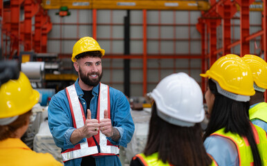 Supervisor and group of factory workers wearing hard hats meeting brief together before starting the day's work.