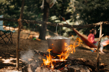 Travel a kettle over a fire burning on the river and sunset backgroun. Cooking over a campfire.