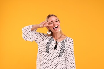 Portrait of hippie woman showing tongue and peace sign on yellow background