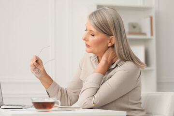 Woman suffering from neck pain at workplace in room