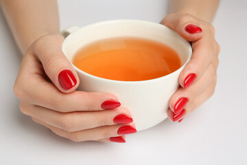 Woman with red polish on nails holding cup of hot drink on white background, closeup