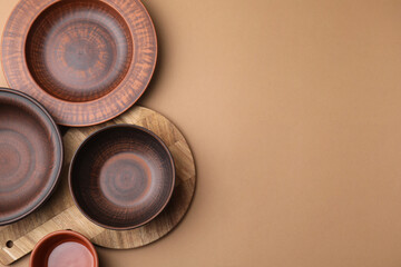 Ceramic bowls, wooden board and plate on beige background, flat lay. Space for text