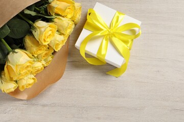 Beautiful bouquet of yellow roses and gift box on wooden table, flat lay. Space for text
