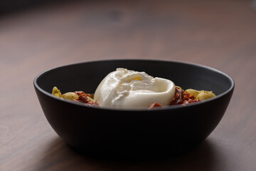Pesto conchiglie with sundried tomatoes and burrata cheese served in black bowl