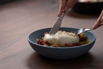 Closeup of pesto conchiglie with sundried tomatoes and cutting burrata cheese served in blue bowl