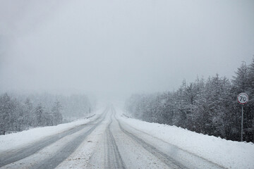 Obraz premium Photo of the winter road during the snowfall in Magadan, Russia. Snow showers on the trees and hills. Slush on the way. Fog and haze, low visibility due to snowstorm. Extreme weather conditions