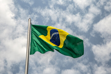 Uma Bandeira do Brasil tremulando ao vento em um dia com muitas nuvens no céu.