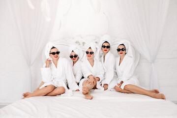 Well-groomed girls get together to celebrate a bachelorette party. Women after spa treatments, wrapping their heads in a towel, enjoy the fun. Concept of entertainment and spa treatments for women.