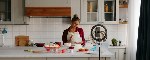 Confident young woman preparing cream for homemade cake and recording video for food blog - obrazy, fototapety, plakaty