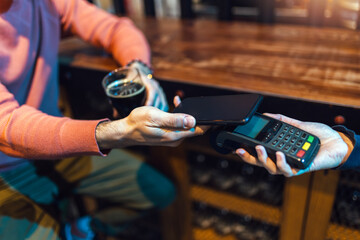 Man in bar paying with cellular device - obrazy, fototapety, plakaty