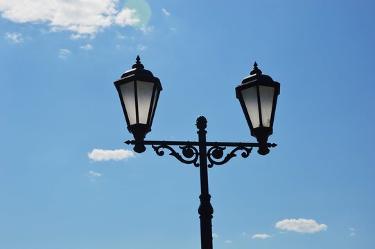 Two black vintage street lamps against a blue sky.
