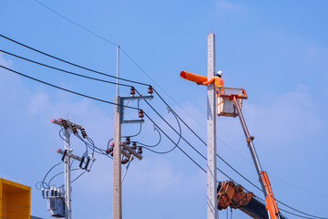 Electrician with crane truck is installing new electrical pole against blue sky background