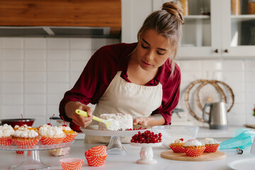 Concentrated female pastry chef applying whipped cream while making a cake at the domestic kitchen