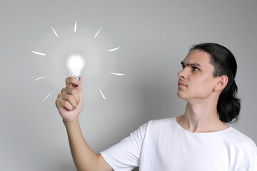 Young man with worried face holds glowing light bulb in his hand. Demonstrates process of solving problem
