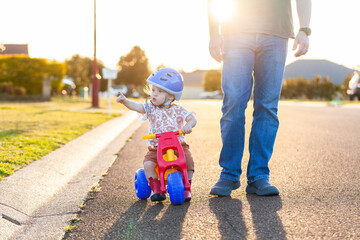 Toddler riding on tricycle bike down suburban road on walk with dad