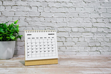 White March 2024 calendar on office wooden desk with potted plant.