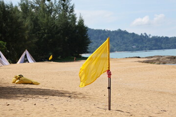 Yellow flag is planted on the beach as a warning sign about safety when swimming in the sea.  The...