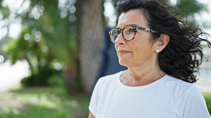 Middle age hispanic woman looking to the side with serious expression at park
