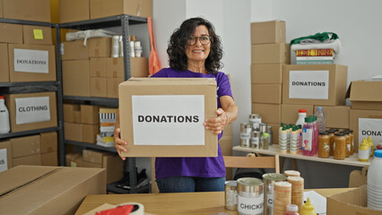Middle age hispanic woman volunteer smiling confident holding donations package at charity center