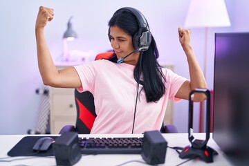 Mature hispanic woman playing video games at home showing arms muscles smiling proud. fitness concept.