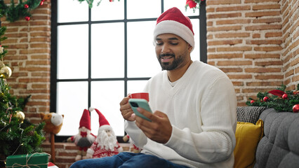 African american man using smartphone drinking coffee celebrating christmas at home
