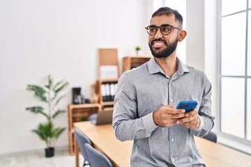 Young hispanic man business worker smiling confident using smartphone at office
