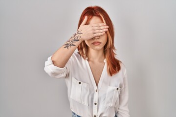 Young caucasian woman standing over isolated background covering eyes with hand, looking serious and sad. sightless, hiding and rejection concept