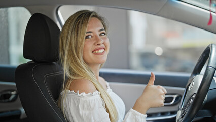 Young blonde woman driving car doing thumb up gesture at street