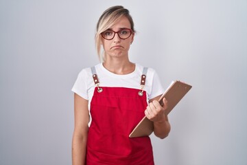 Young blonde woman wearing waiter uniform holding clipboard depressed and worry for distress,...