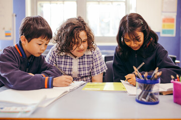 Three school students sitting at their desk in the classroom working