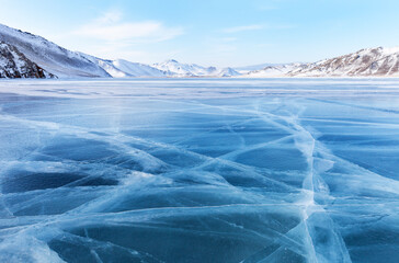 Scenic winter landscape of frozen Baikal Lake on cold sunny February day. Shallow bay is covered with blue ice with cracks against backdrop of snowy coastal mountains. Beautiful natural background - obrazy, fototapety, plakaty