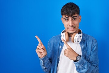 Young hispanic man standing over blue background pointing aside worried and nervous with both hands, concerned and surprised expression