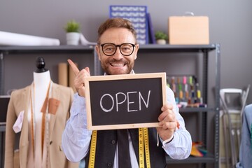 Middle age man with beard dressmaker designer holding open sign smiling happy pointing with hand and finger to the side