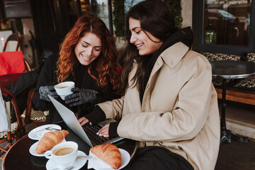 hispanic business couple of women working and using laptop at coffee shop in winter in an urban...