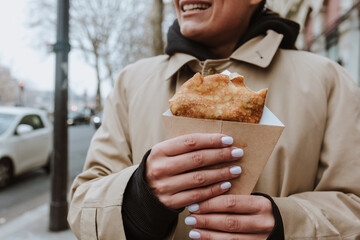 hispanic woman eating delicious crepes in the streets of Paris city, hands holding pancakes  - Powered by Adobe