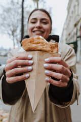 hispanic woman eating delicious crepes in the streets of Paris city, hands holding pancakes 